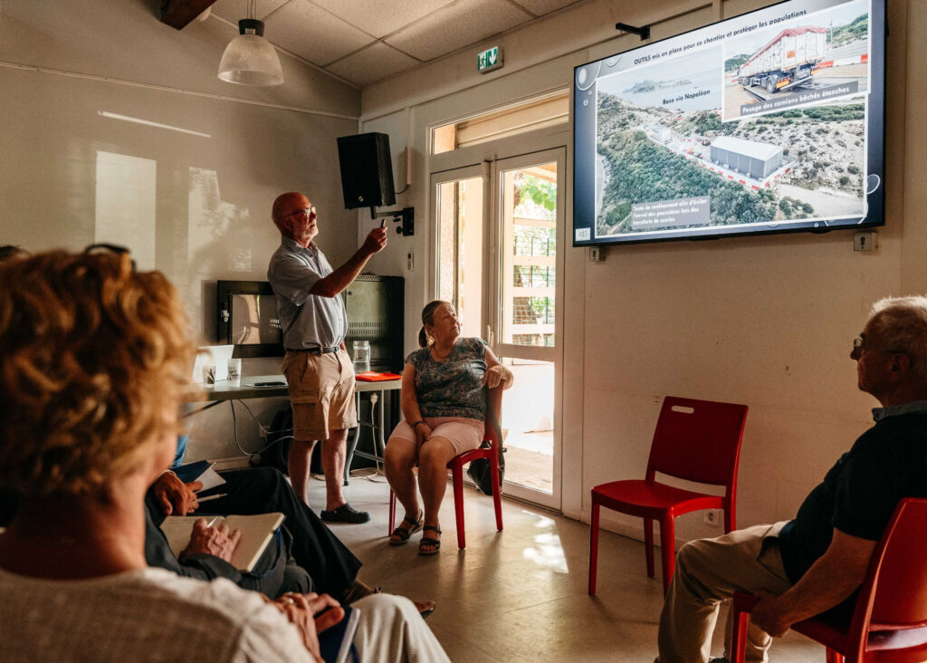 In una riunione pubblica dell’ASLS a giugno 2026, i membri dell’associazione – tra cui il presidente Rolland Dadena, a destra – mostrano il contrasto tra i lavori realizzati nel Parco Nazionale dei Calanchi e lo stato di abbandono del sito inquinato di Legré-Mante. | Foto: ©Maïté Baldi